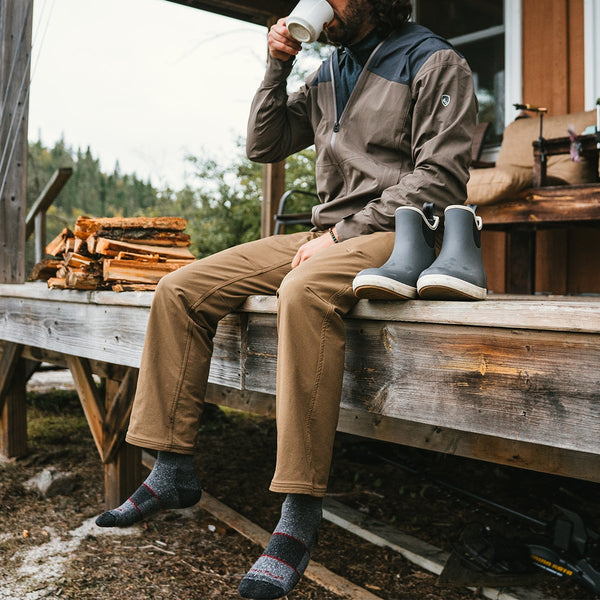 Person sitting on a wooden deck with a cup, surrounded by nature