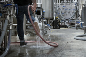 Person wearing The DRY Brand Starboard 6" Deck Boots spraying down a brewery floor with a hose, water splashing mid-step.
