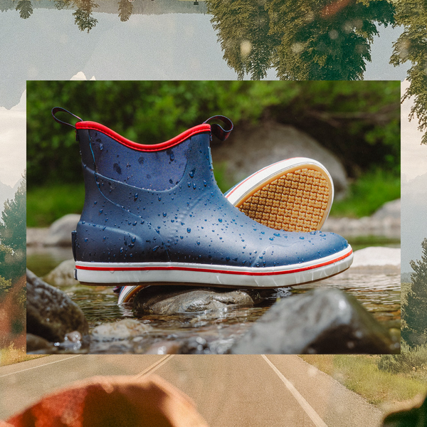 A pair of blue water-resistant rain boots with red trim and white soles, shown standing in shallow water with one boot turned to display the treaded outsole. The boots are centered within a collage-style background featuring a road, trees, and a hat.